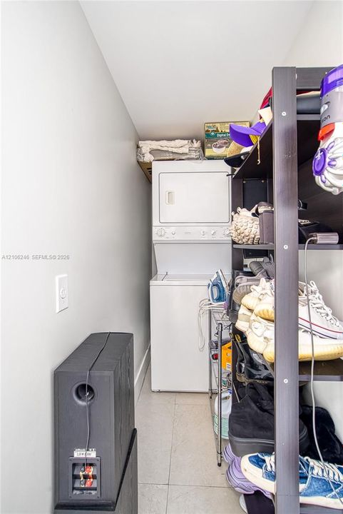 Dedicated laundry area featuring a stacked washer and dryer unit and neutral floor tiling
