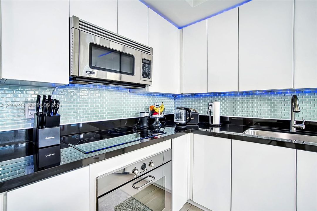 Modern kitchen featuring flat-panel white cabinetry, contrasting black countertops, glass subway tile backsplash, stainless steel built-in microwave, and stainless steel oven