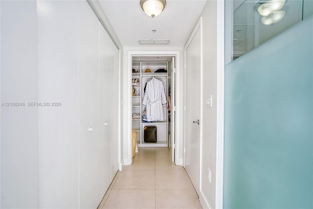 Hallway featuring large-format tile flooring, ceiling-mounted light fixtures, extensive floor-to-ceiling built-in cabinetry, and a walk-in closet with integrated shelving