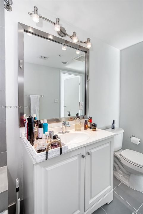 White vanity featuring a smooth countertop with an integrated basin, polished metal hardware, a large framed mirror, and four-light vanity fixture