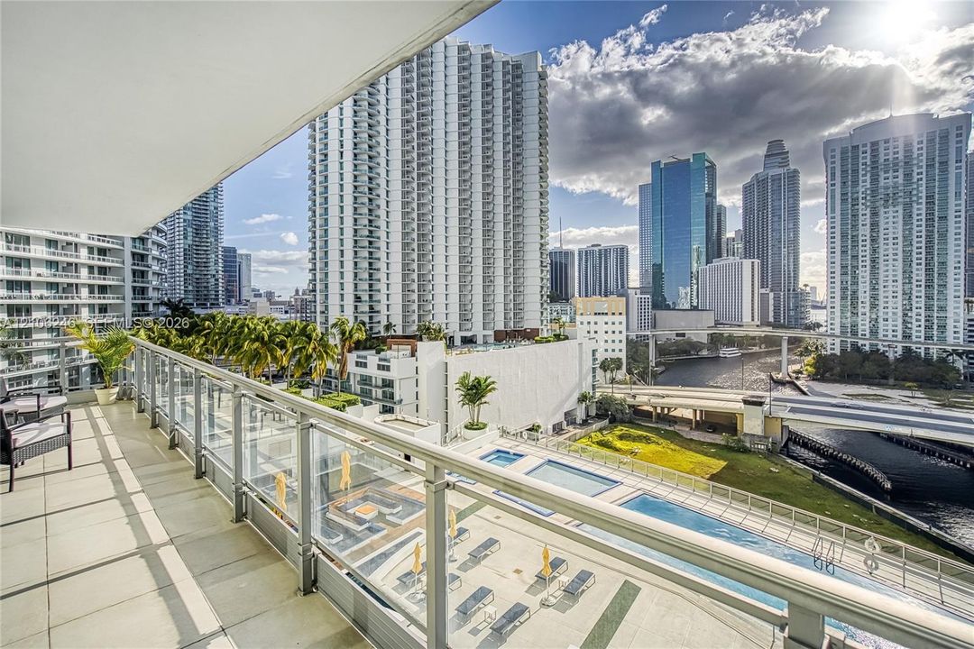 Covered balcony featuring tile flooring and a glass-paneled railing overlooking an urban skyline and multi-level swimming pools