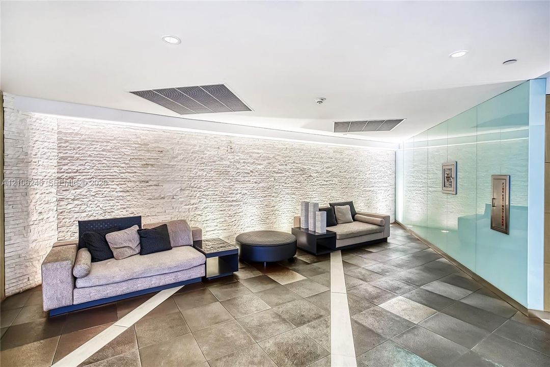 Curved stone-textured accent wall with integrated LED uplighting, large-format tile flooring with contrasting linear inlays, and floor-to-ceiling glass paneling