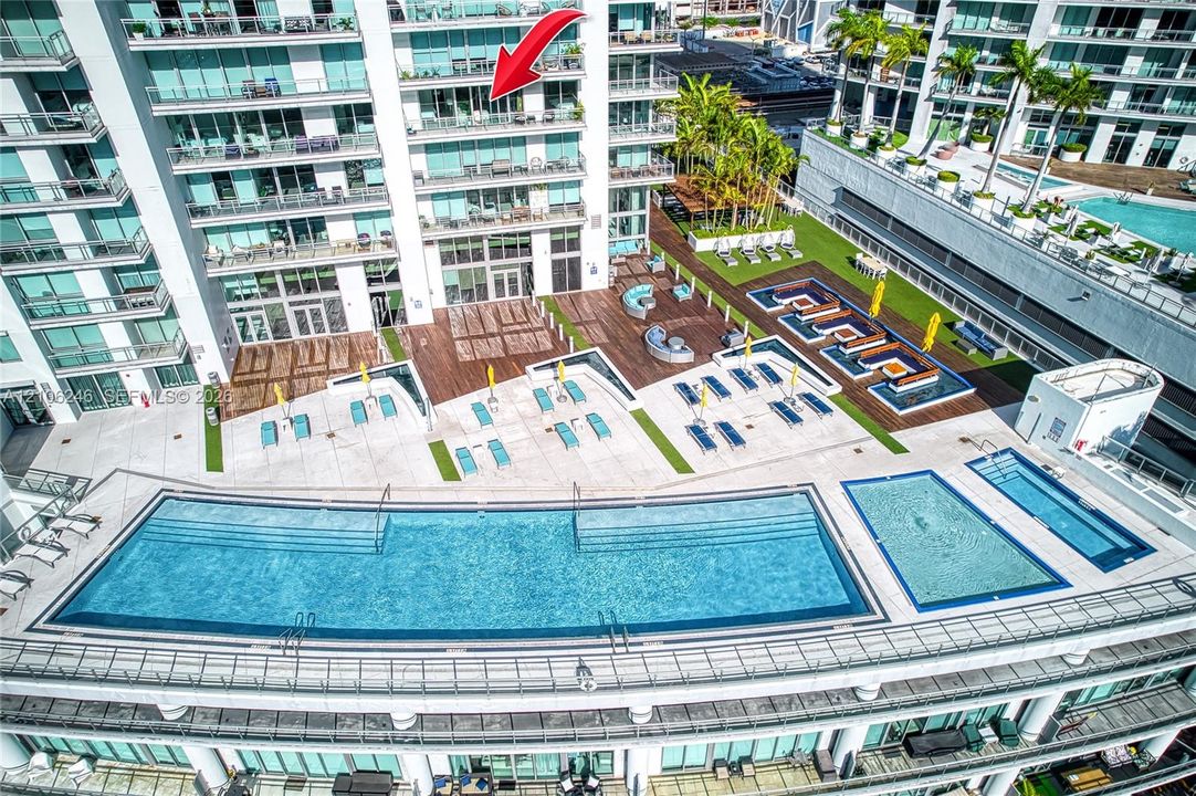 Elevated terrace balcony featuring floor-to-ceiling glass panel doors, exterior swimming pool, multi-level sundeck, and landscaped grounds