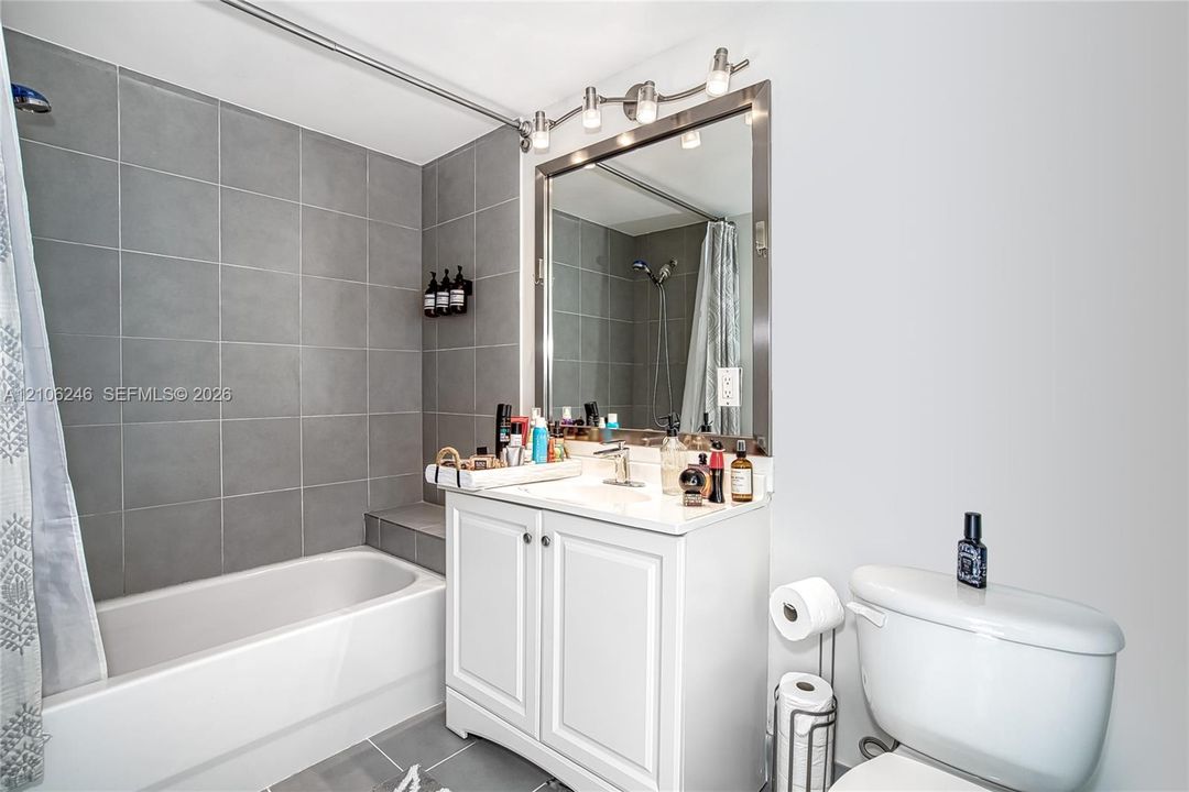 Bathroom featuring a white vanity with built-in cabinetry, a rectangular basin with a single-handle faucet, a framed mirror, a multi-bulb vanity light fixture, and a tiled bathtub surround