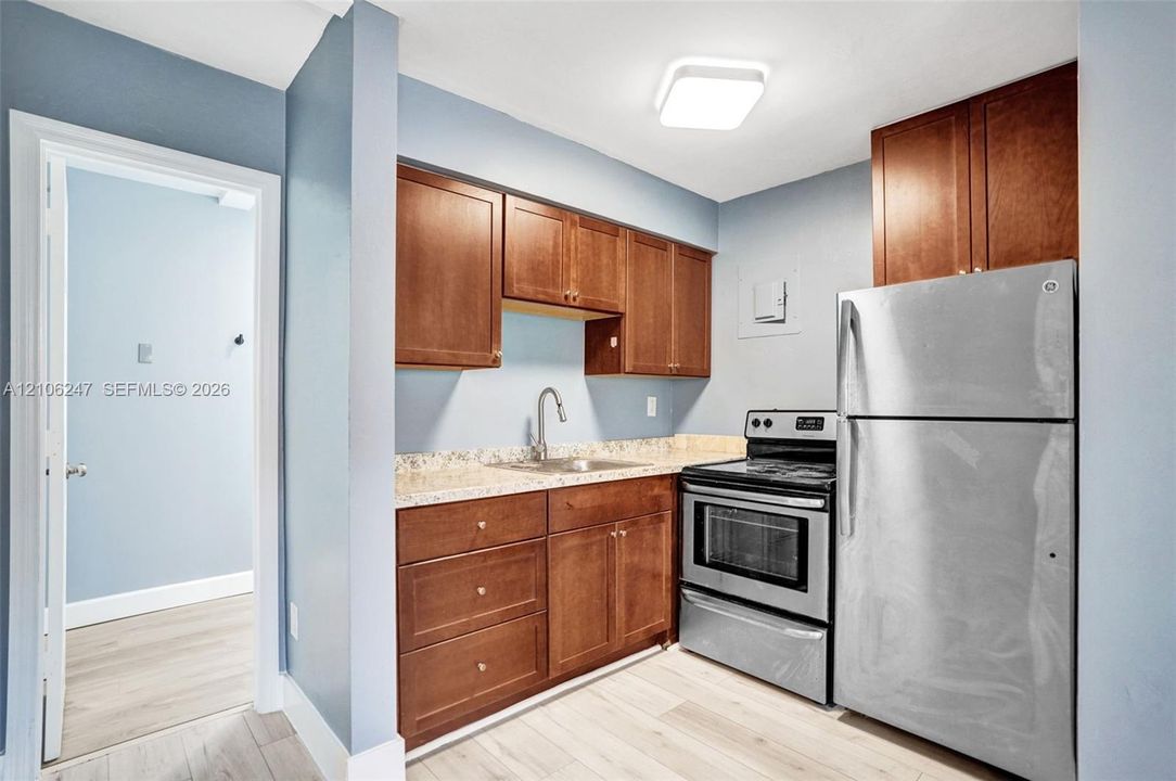 Kitchen featuring wood cabinetry, stone-finish countertops, stainless steel appliances, and a gooseneck faucet
