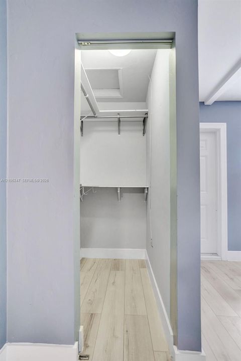Walk-in closet featuring tiered white shelving, a metal hanging rod, and wood-finish flooring