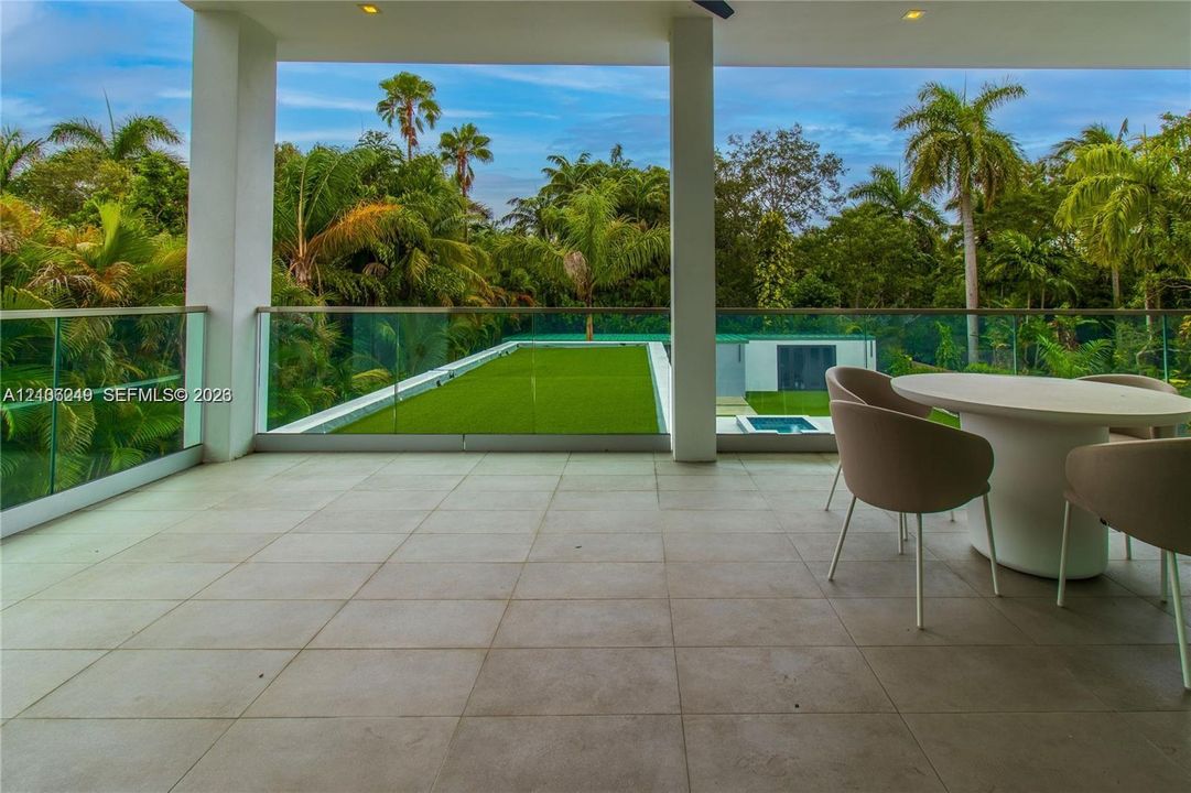 Covered terrace featuring large-format stone-style tile flooring, glass panel railings, and recessed ceiling lighting