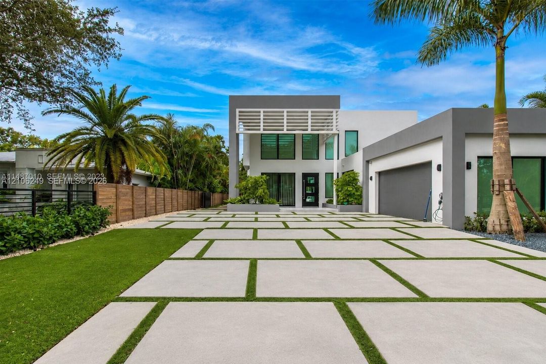 Contemporary two-story exterior featuring a geometric concrete paver driveway with integrated turf, tiered architectural facade, dual-tone masonry, and attached garage