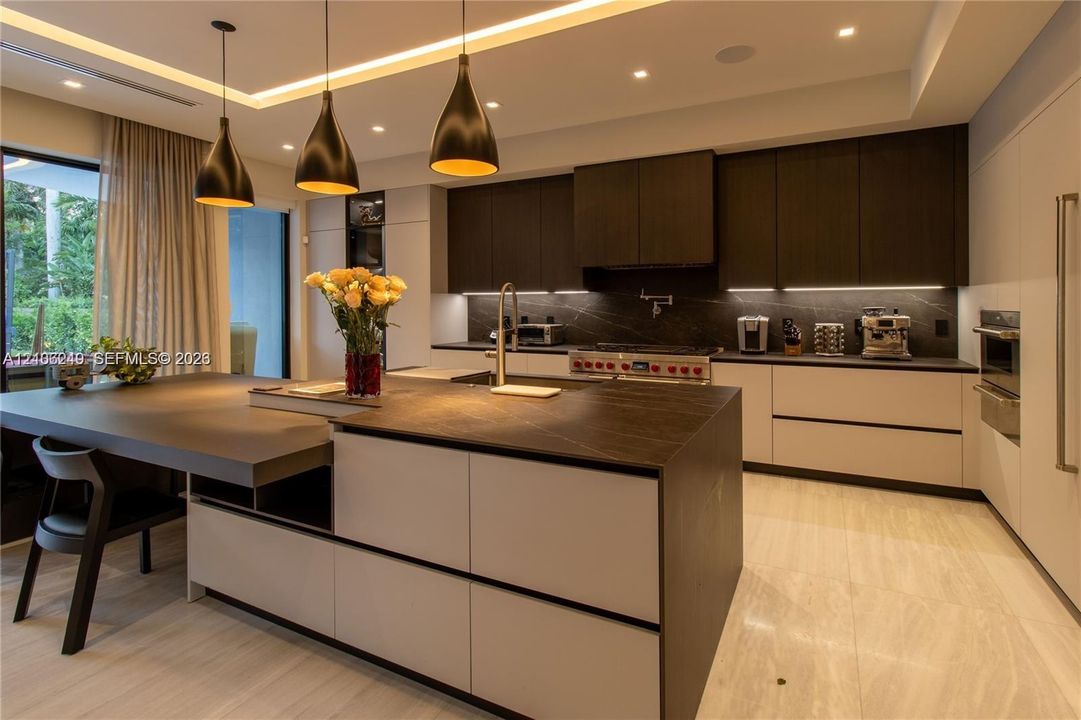 Gourmet kitchen featuring a large central island with stone-finish countertops, matte-finish cabinetry, built-in dual wall ovens, and custom pendant lighting