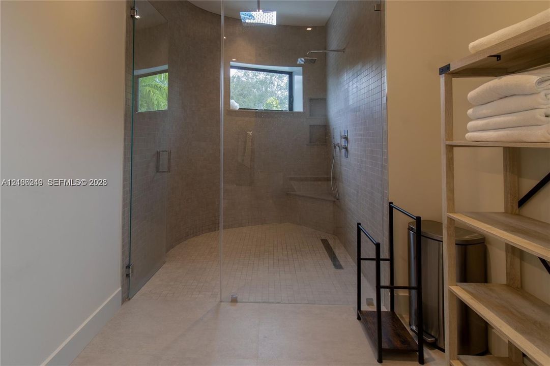 Walk-in shower featuring a glass enclosure, wall-mounted rain shower head, built-in tiled bench, recessed wall shelving, and a linear floor drain