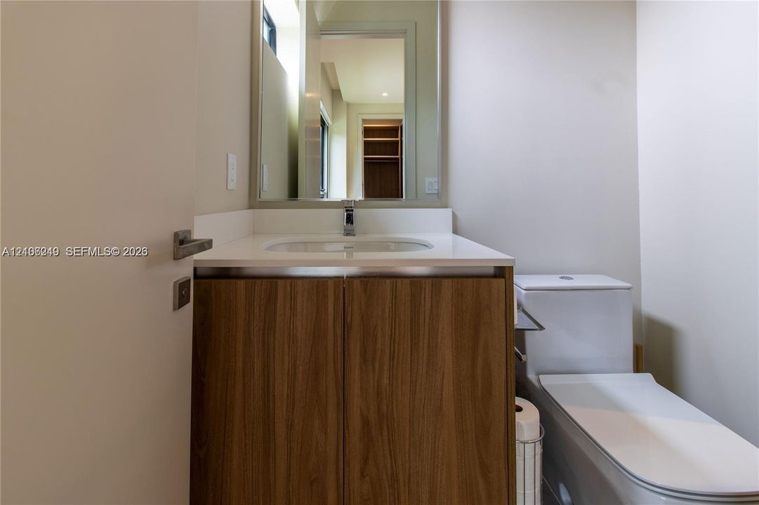 Vanity featuring a wood-finish cabinet, white countertop with an integrated basin, wall-mounted mirror, and chrome faucet