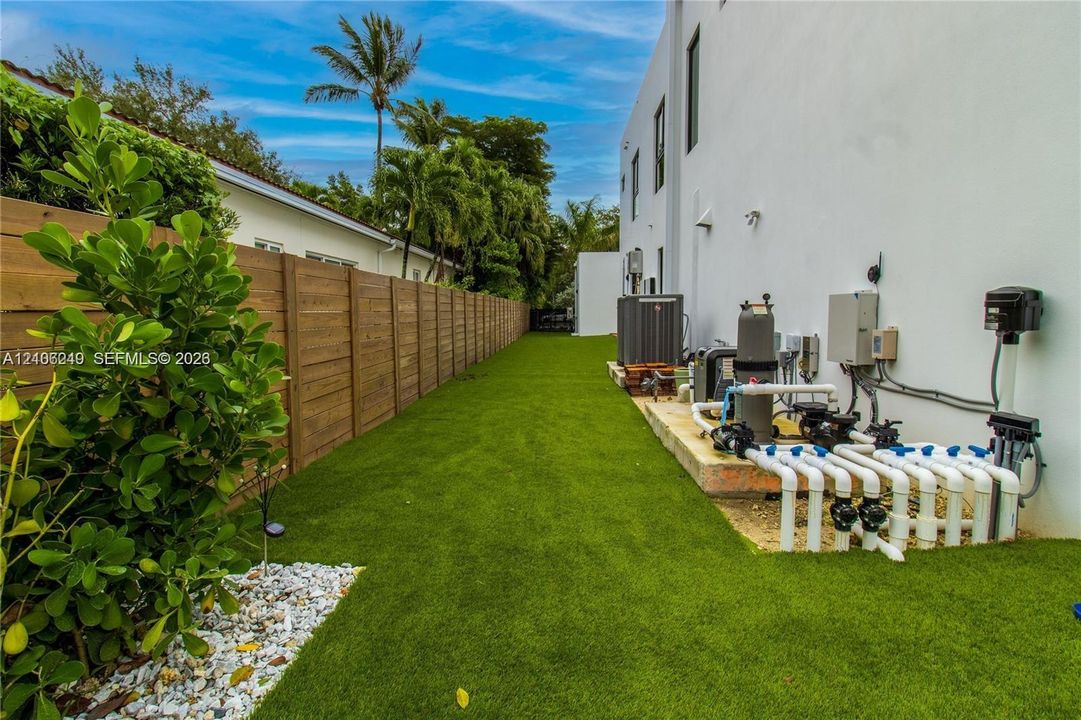 Side yard featuring synthetic turf, wood-plank privacy fencing, and exterior mechanical systems including pool equipment and HVAC unit