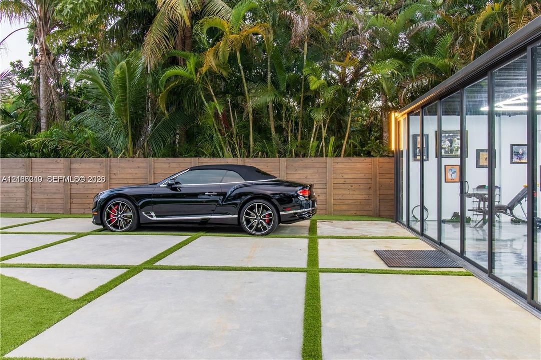 Large-format concrete paver driveway with turf infill, horizontal wood privacy fencing, and floor-to-ceiling glass wall panels