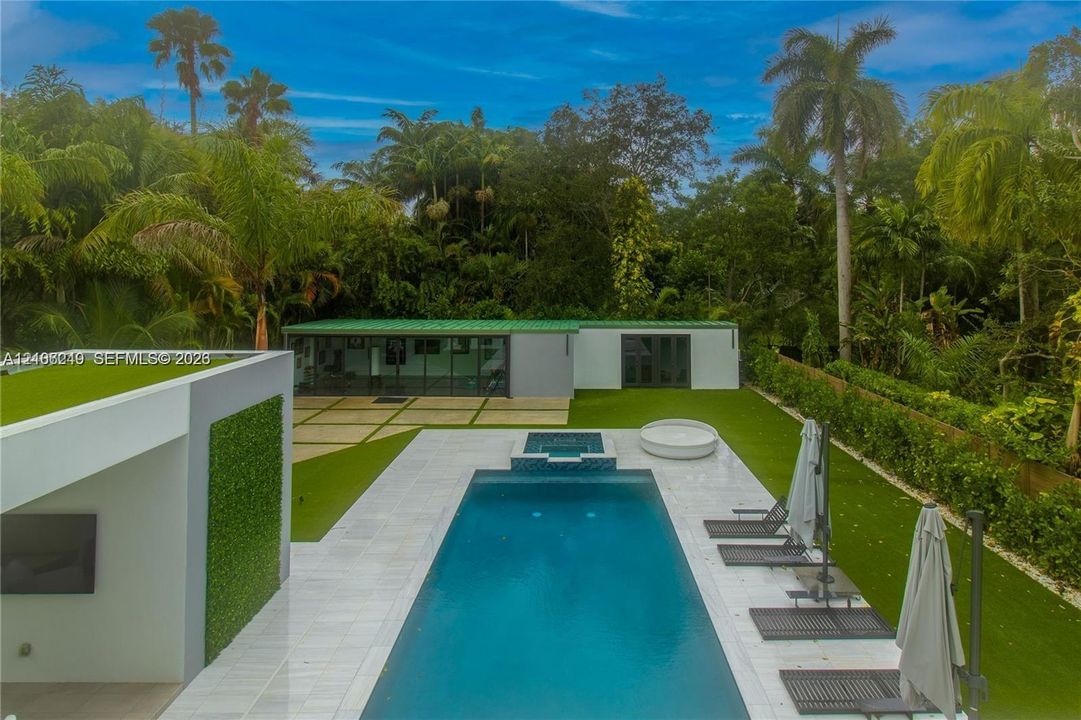 Outdoor space featuring an in-ground swimming pool with integrated spa, white stone pool deck, synthetic lawn, and a detached structure with metal roofing