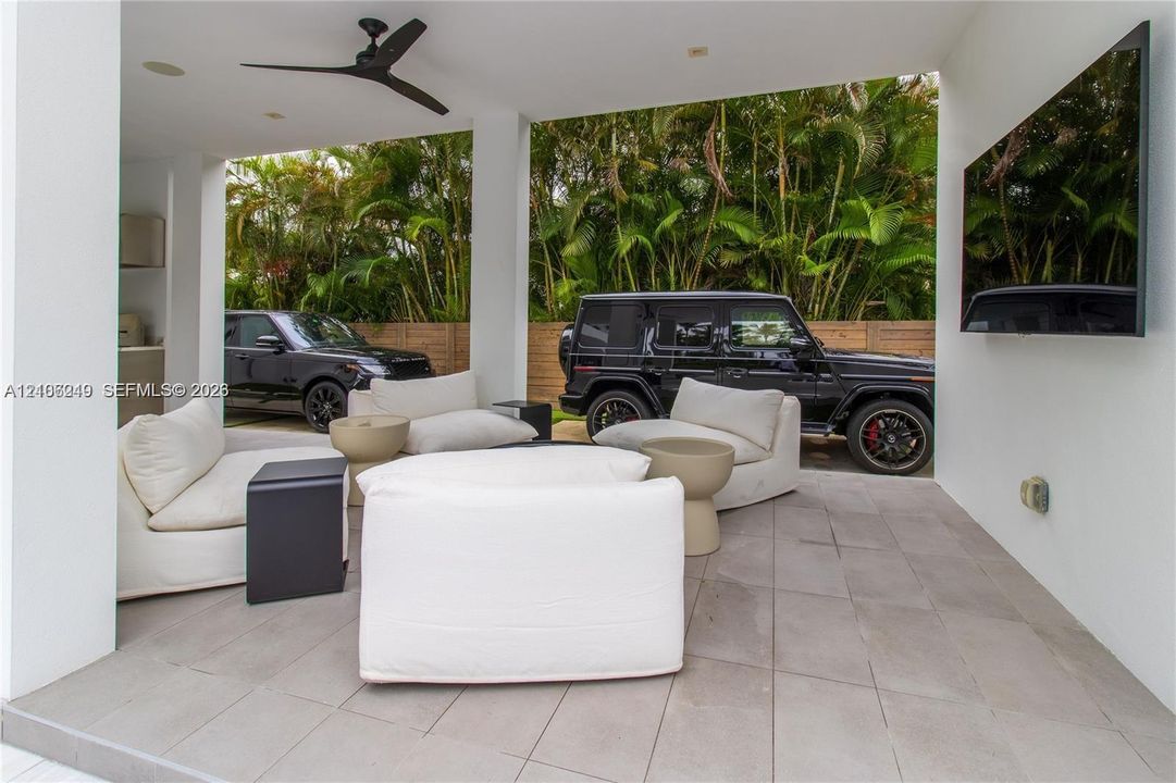 Covered outdoor space featuring large-format tile flooring, recessed lighting, a matte black ceiling fan, and wall-mounted television interface