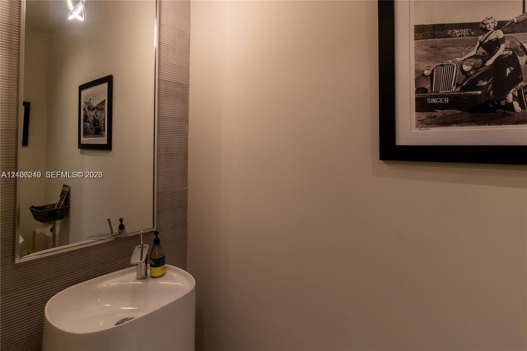 Modern powder room featuring a streamlined oval vessel sink, chrome single-handle faucet, oversized rectangular wall mirror, and textured tile wall accent