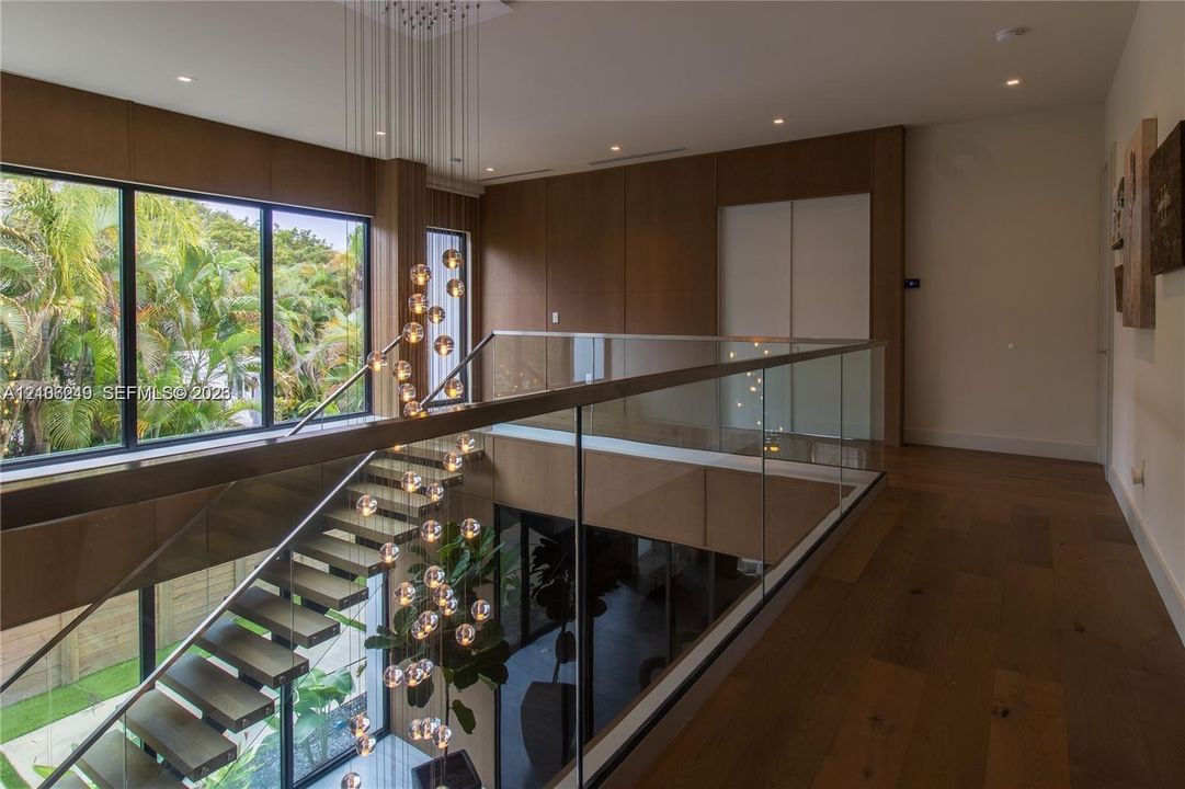 Floating staircase with wood treads and glass railing, large-format wood-finish wall paneling, floor-to-ceiling windows, recessed lighting, and wood-finish flooring