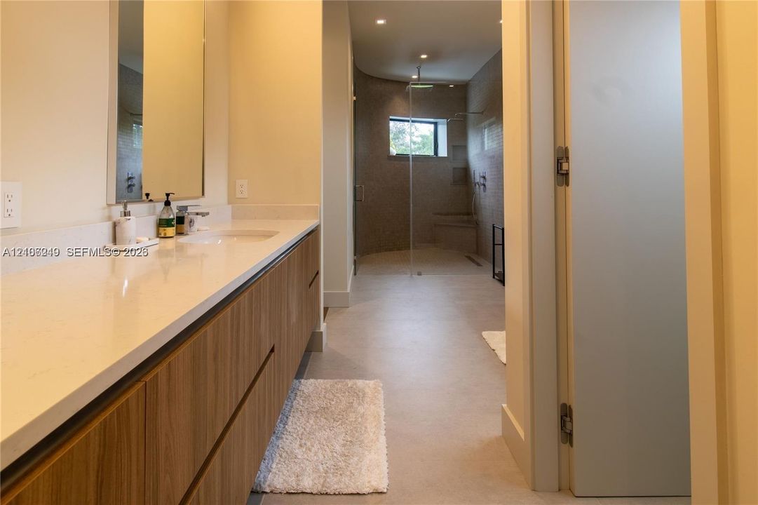 Floating vanity with a wood-finish, integrated countertop with a sink, large frameless mirror, and a walk-in shower with tiled walls and a built-in bench