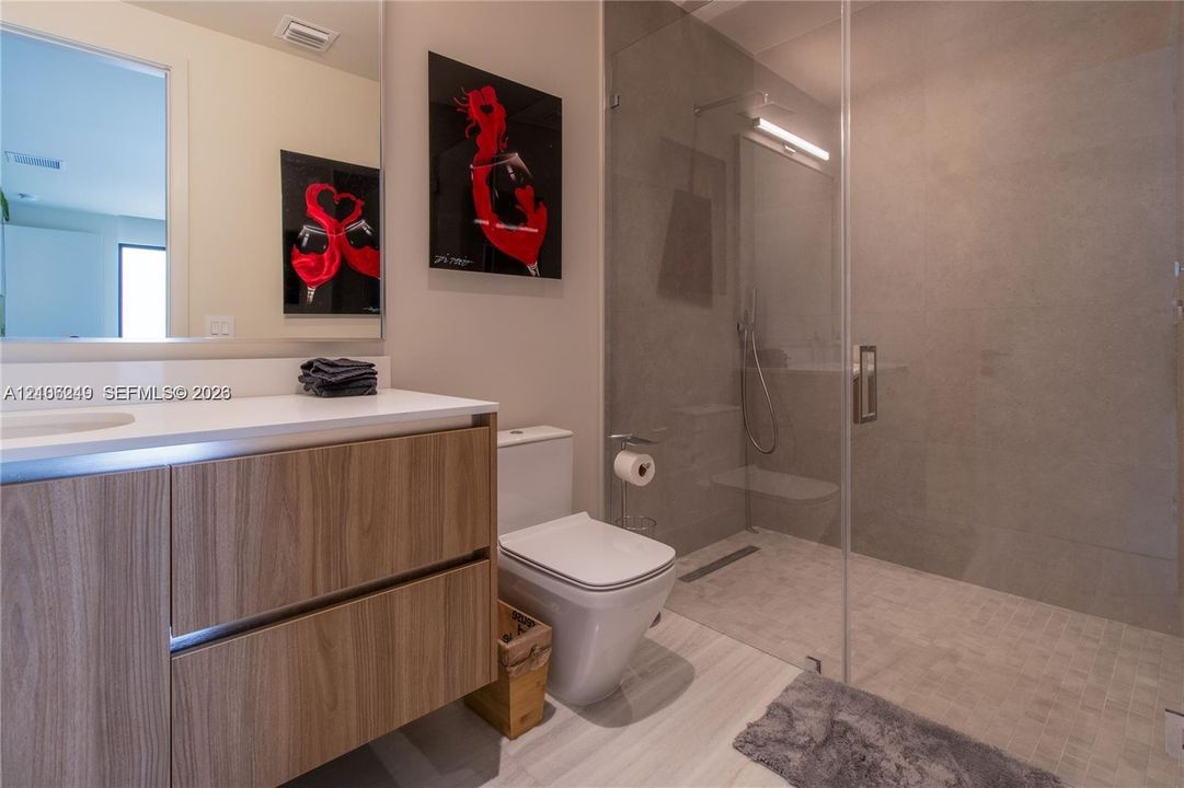 Modern bathroom featuring a wood-finish vanity with a white countertop, walk-in shower with floor-to-ceiling tile, frameless glass enclosure, and a wall-to-wall mirror