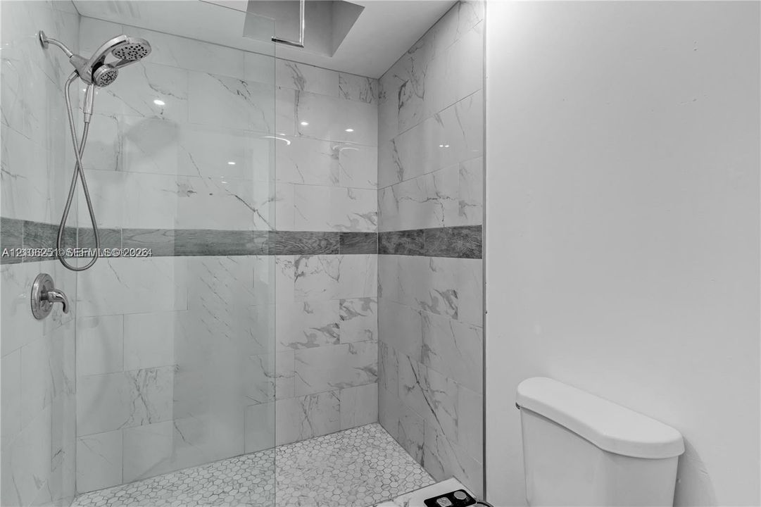 Walk-in shower featuring floor-to-ceiling stone-finish wall tile, a horizontal decorative accent border, pebble-style floor tiling, a frameless glass enclosure, and a multi-function shower head