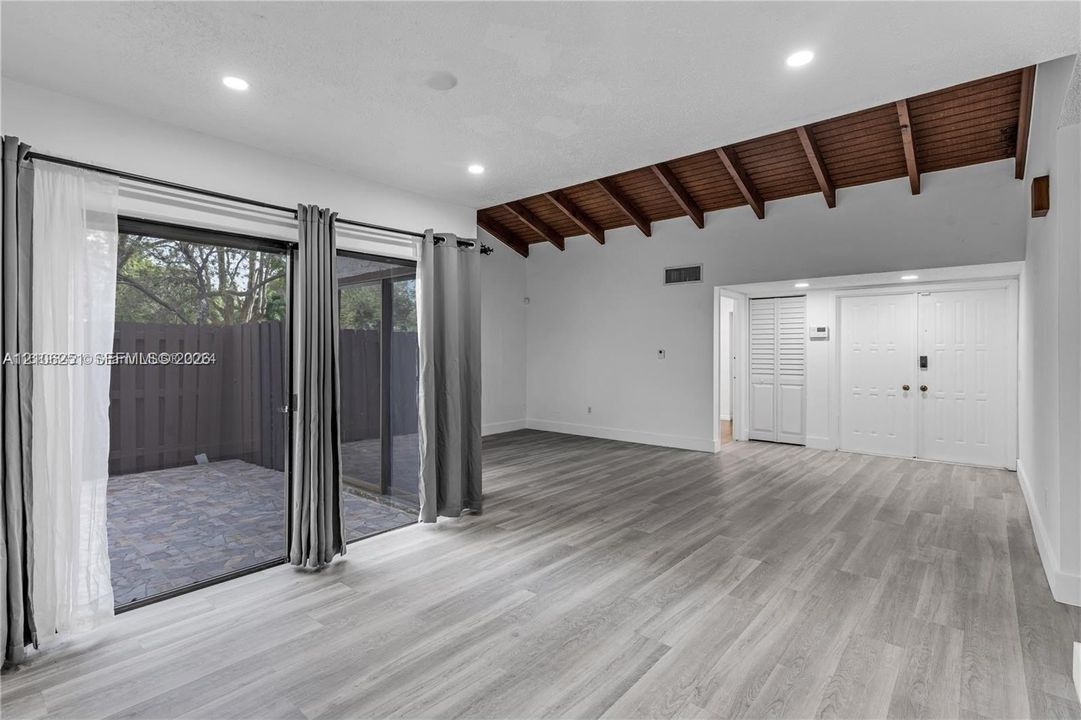 Living area featuring vaulted exposed wood-beam ceilings, wood-finish flooring, recessed lighting, double-door entry, and floor-to-ceiling sliding glass doors