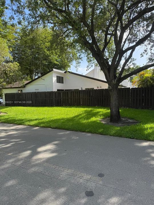 Exterior featuring a white stucco facade, a dark-toned vertical wood privacy fence, and a mature landscape with established trees
