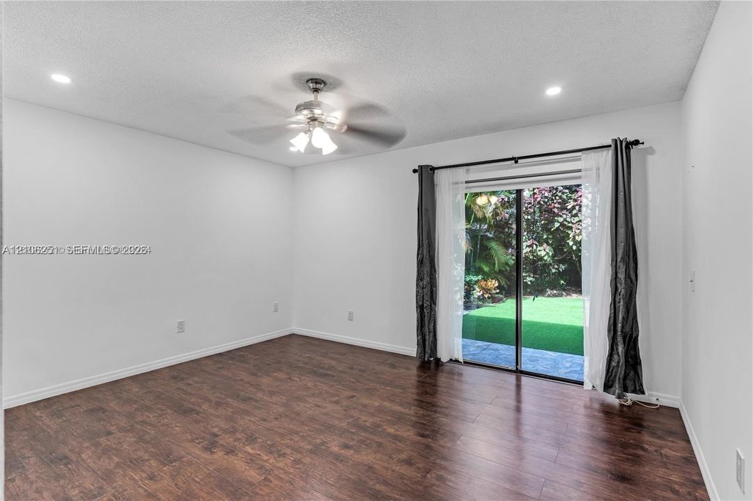 Wood-finish flooring, recessed lighting, ceiling fan with light fixture, and sliding glass door with exterior access to a paved patio and artificial turf