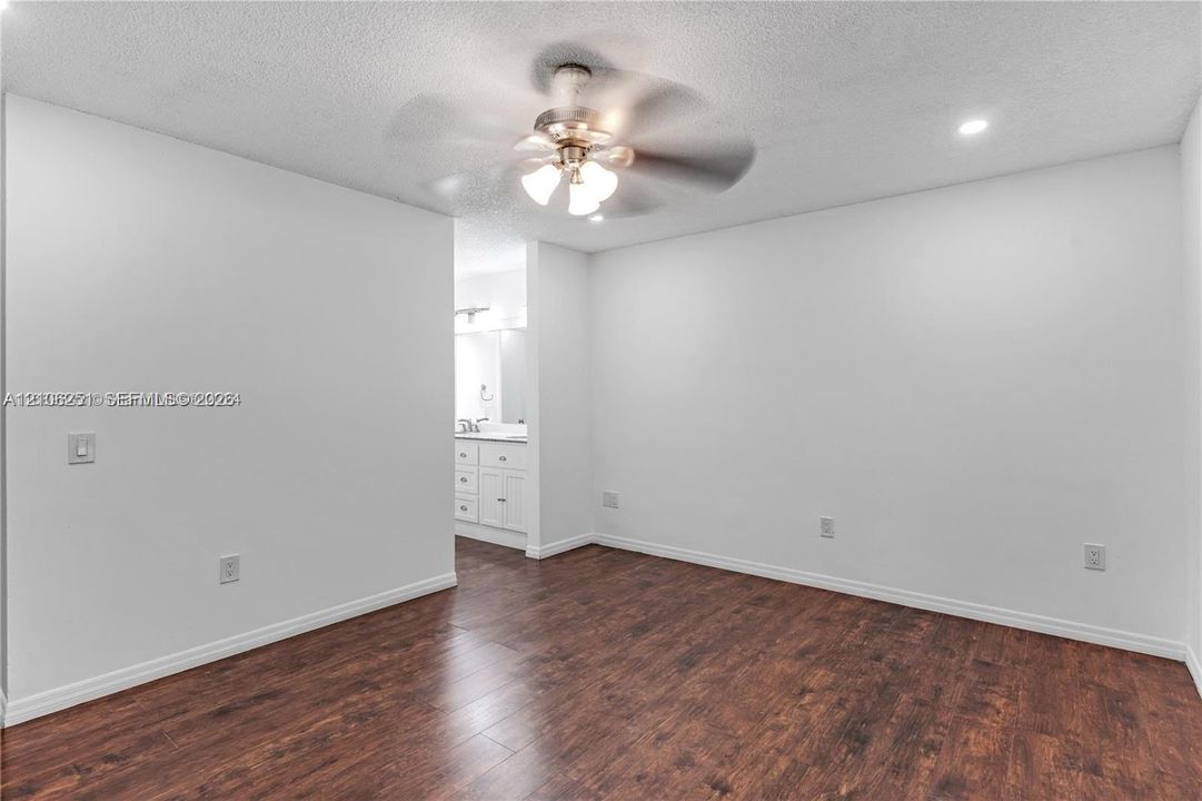 Neutral-toned interior room featuring wood-finish flooring, a ceiling fan with integrated lighting, and recessed ceiling lighting