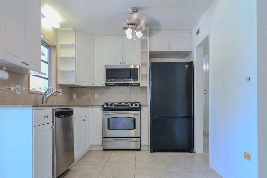 Kitchen featuring white cabinetry with open shelving, stone-finish countertops, tile flooring, and stainless steel appliances
