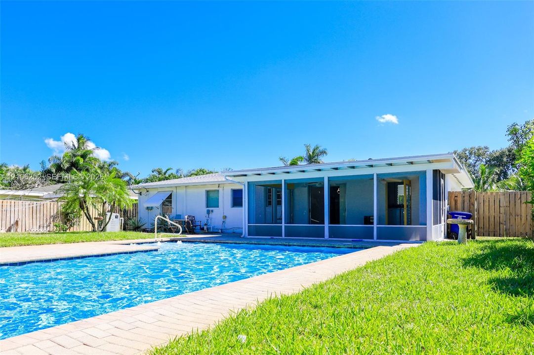 Rear exterior featuring an in-ground swimming pool, brick paver decking, a screened-in lanai, and wood-style privacy fencing