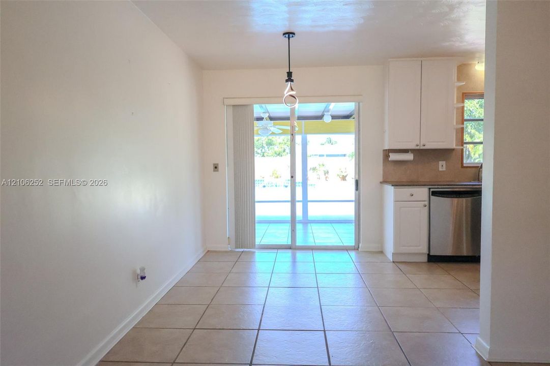 Ceramic tile flooring, white cabinetry, stainless steel dishwasher, and sliding glass doors with overhead pendant lighting