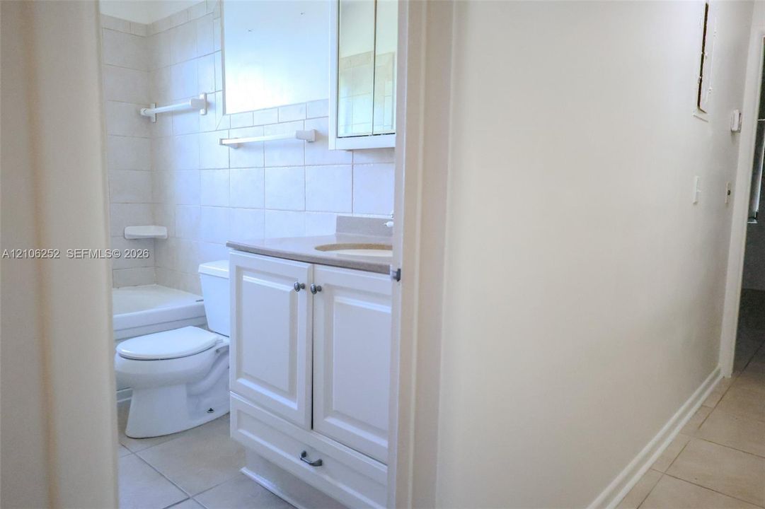 Bathroom featuring a white vanity cabinet with an integrated countertop and sink, a mirrored medicine cabinet, a standard toilet, and a tiled tub surround