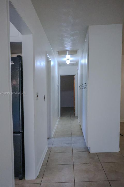 Hallway featuring tile flooring, ceiling-mounted lighting, and floor-to-ceiling built-in white cabinetry