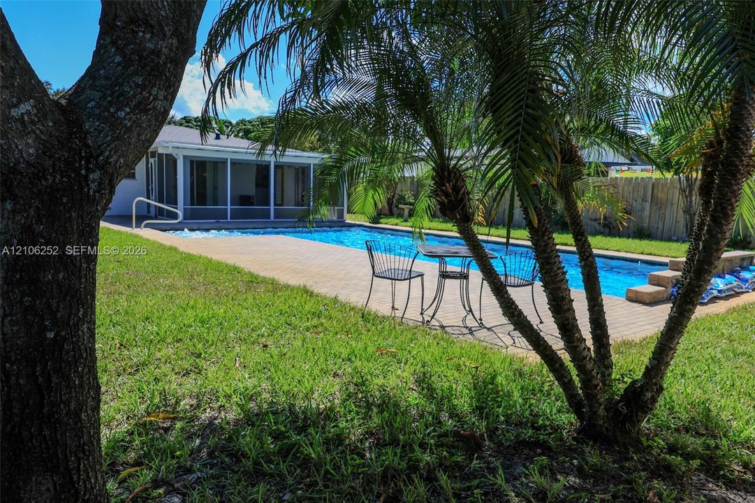 Rectangular swimming pool with paver decking, screened-in porch, and perimeter fencing