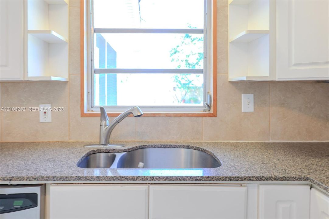 Kitchen featuring stone-finish countertops, stainless steel undermount sink with a gooseneck faucet, light-toned ceramic tile backsplash, and white cabinetry with open shelving