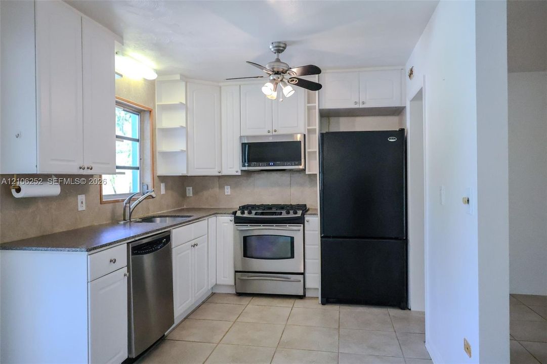 Kitchen featuring white shaker-style cabinetry, neutral stone-finish countertops, tile flooring, and integrated stainless steel and black appliances