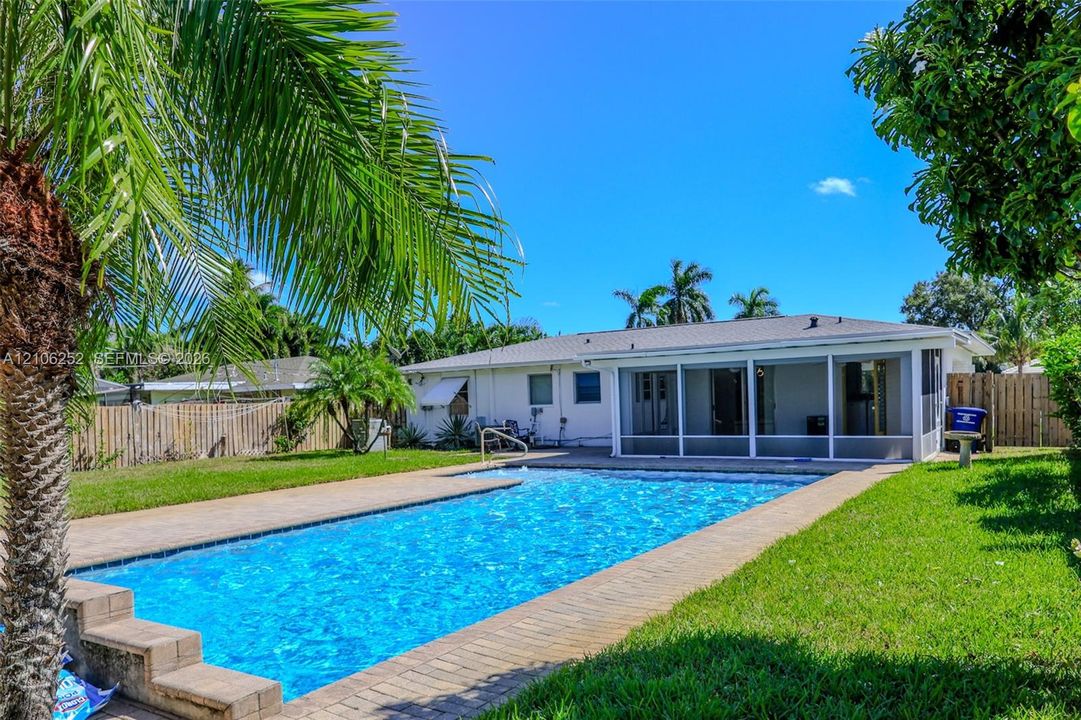Private backyard featuring a rectangular swimming pool, paver patio surround, screen-enclosed porch, and wood privacy fencing