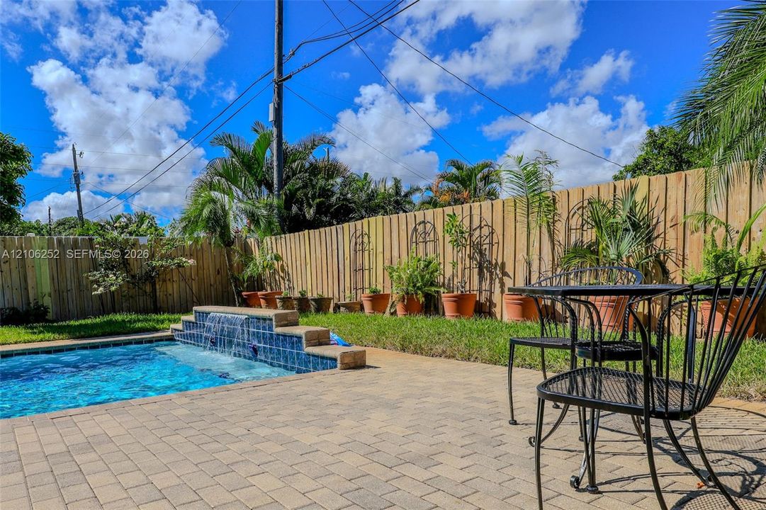 Backyard featuring an in-ground swimming pool with a tiered tile waterfall, stone paver decking, and a wood privacy fence