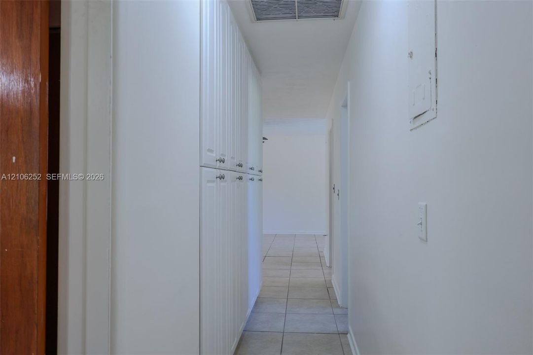 Hallway featuring full-height white cabinetry with nickel hardware, neutral tile flooring, and a ceiling-mounted skylight