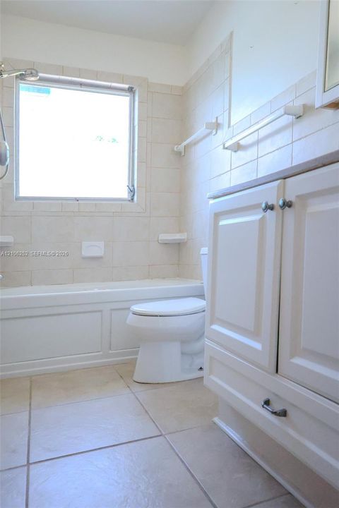 Bathroom featuring white cabinetry, tile flooring, wall-mounted towel bars, and a built-in tub with tile surround