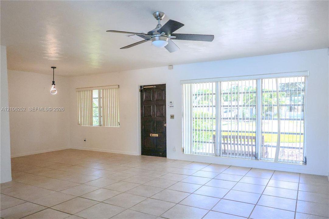 Living area featuring large-format ceramic tile flooring, a multi-blade ceiling fan with integrated light, a paneled wood entry door, and expansive floor-to-ceiling windows