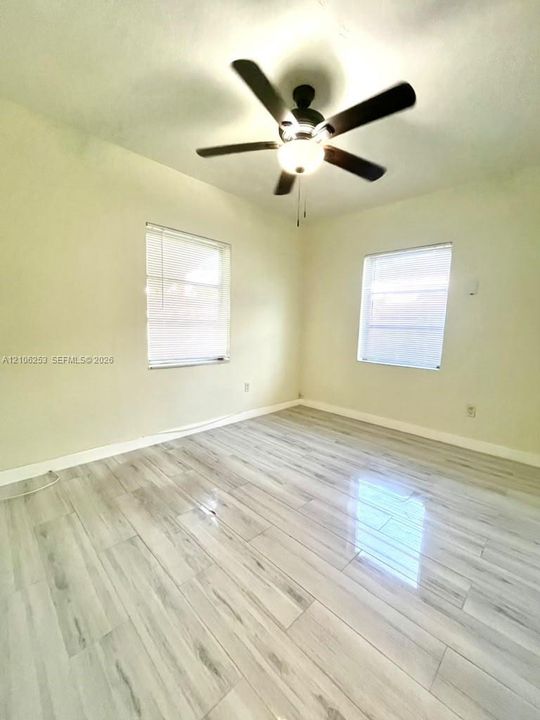 Room featuring porcelin wood-finish flooring, two windows with horizontal blinds, and a central ceiling fan with an integrated light fixture