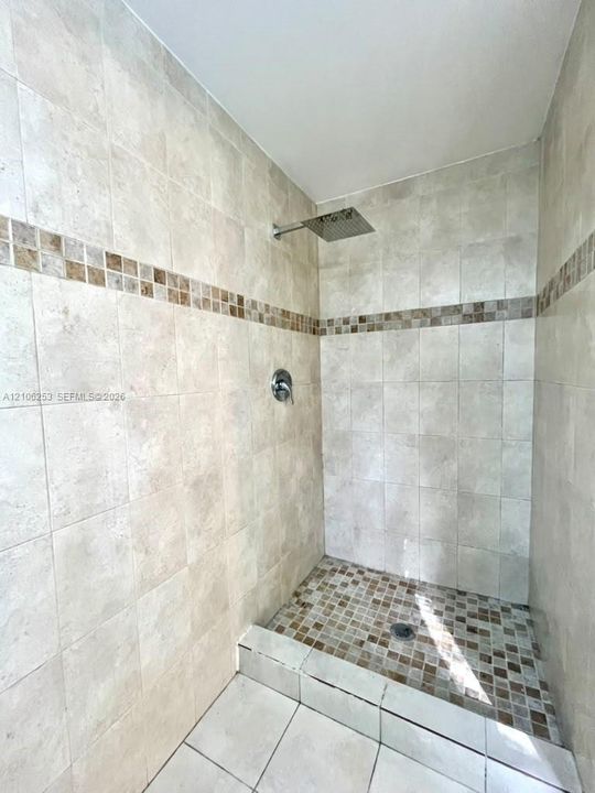 Walk-in shower featuring floor-to-ceiling tile, decorative mosaic tile accents, a square rainfall showerhead, and a mosaic-tiled shower floor