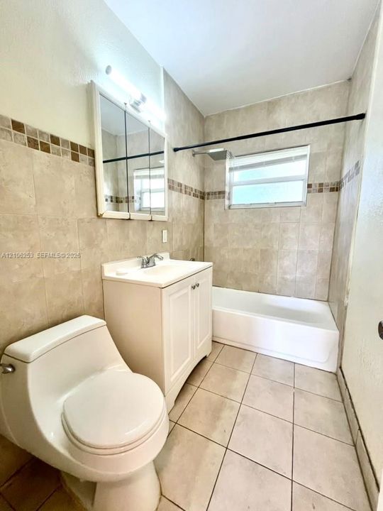 Bathroom featuring a white vanity cabinet with a integrated sink, neutral wall tiling with a mosaic accent border, ceramic floor tiles, a mirrored medicine cabinet, and a shower-tub combination
