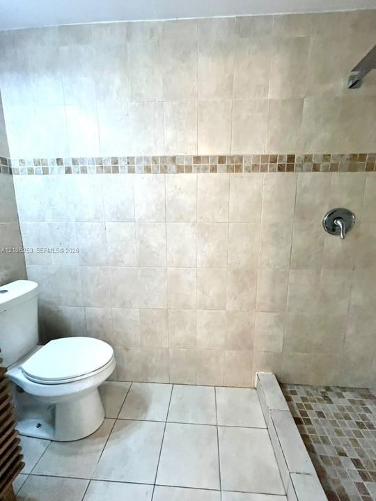 Large-format neutral wall tiling with a mosaic accent border, walk-in shower area, and chrome single-handle shower faucet