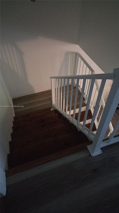 Staircase featuring dark-stained wooden treads, white railing with vertical balusters, and grey wood-finish flooring