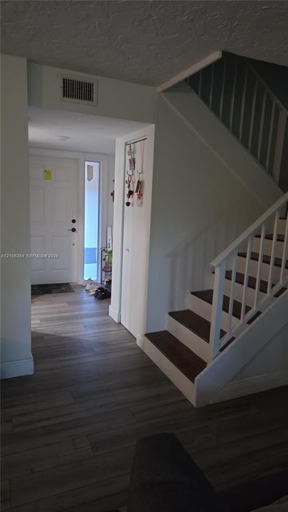 Entryway featuring wood-finish flooring, a white paneled front door with a side light window, and a staircase with white balusters and dark-toned treads
