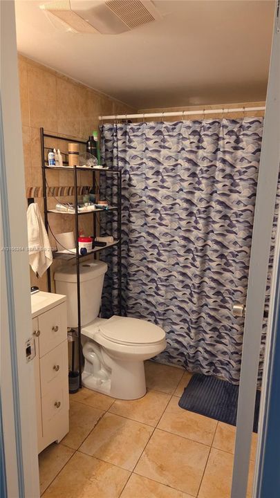 Bathroom featuring light-toned ceramic floor tiling, wall-mounted shower enclosure, white vanity cabinet, and neutral wall tile surround