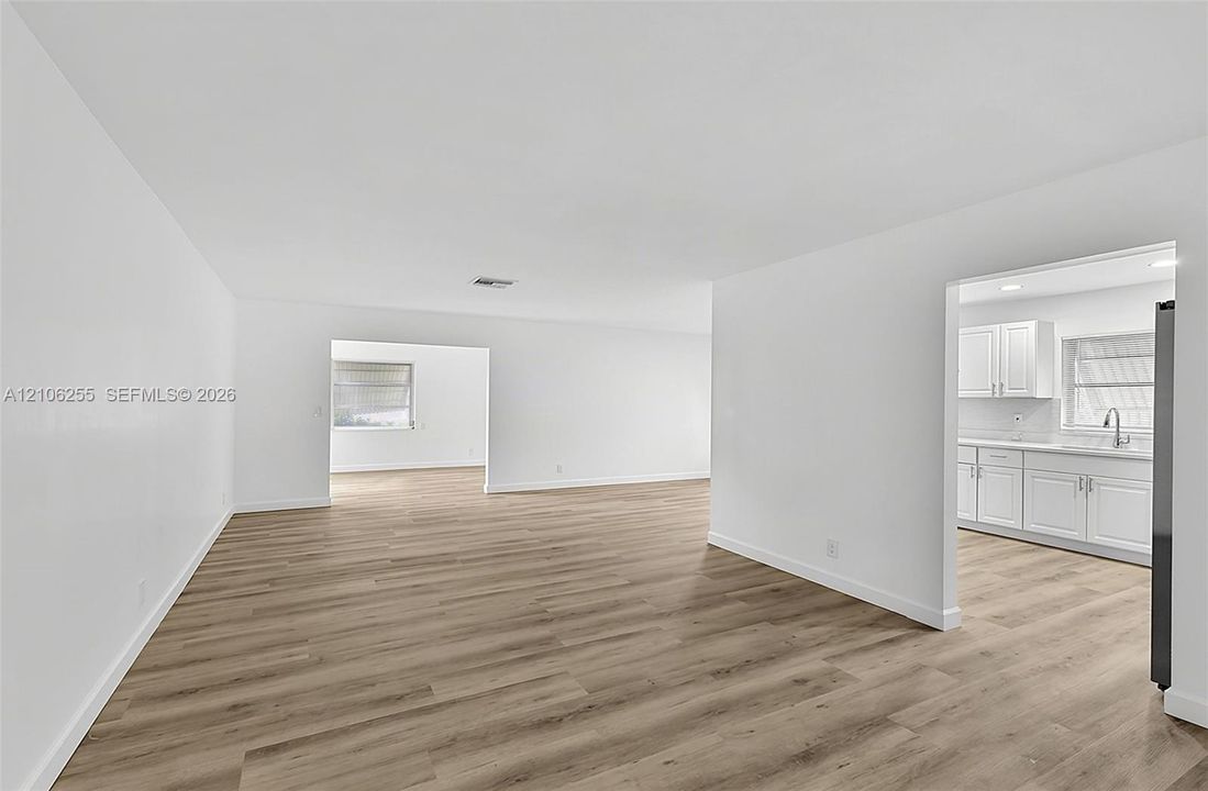 Open interior space featuring wood-finish flooring, white walls, and a kitchen area with white cabinetry and a stainless steel faucet