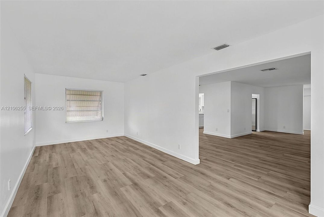 Interior space featuring light-toned wood-finish flooring, crisp white walls, and multiple windows with louvered shades